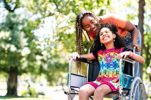 a little girl in a wheelchair enjoying a walk at the park with her mother. a little girl in a wheelchair enjoying a walk at the park with her mother.